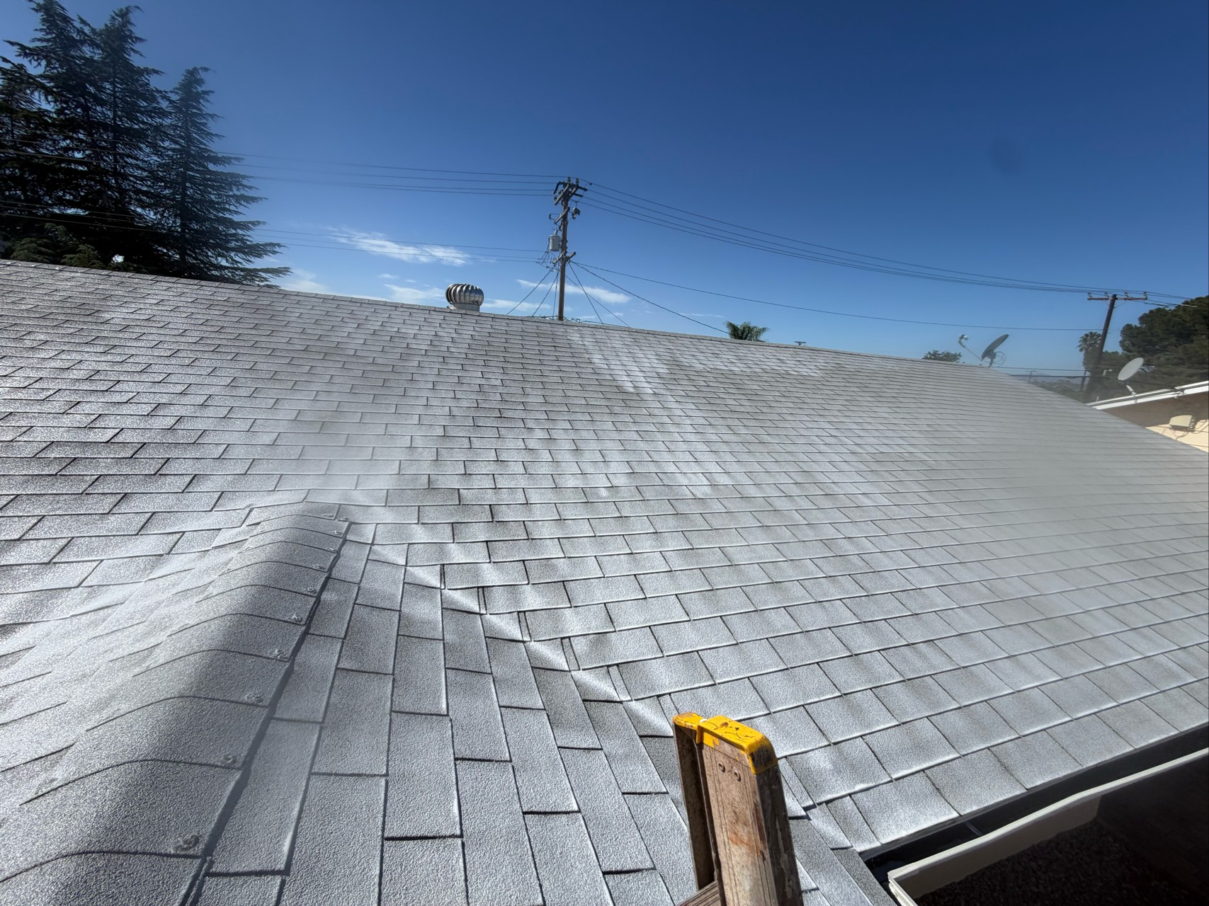 Menifee roof after GreenSoy restoration: asphalt composition shingles carrying a light, reflective coating, with a turbine vent on the ridge and a ladder still set at the gutter.