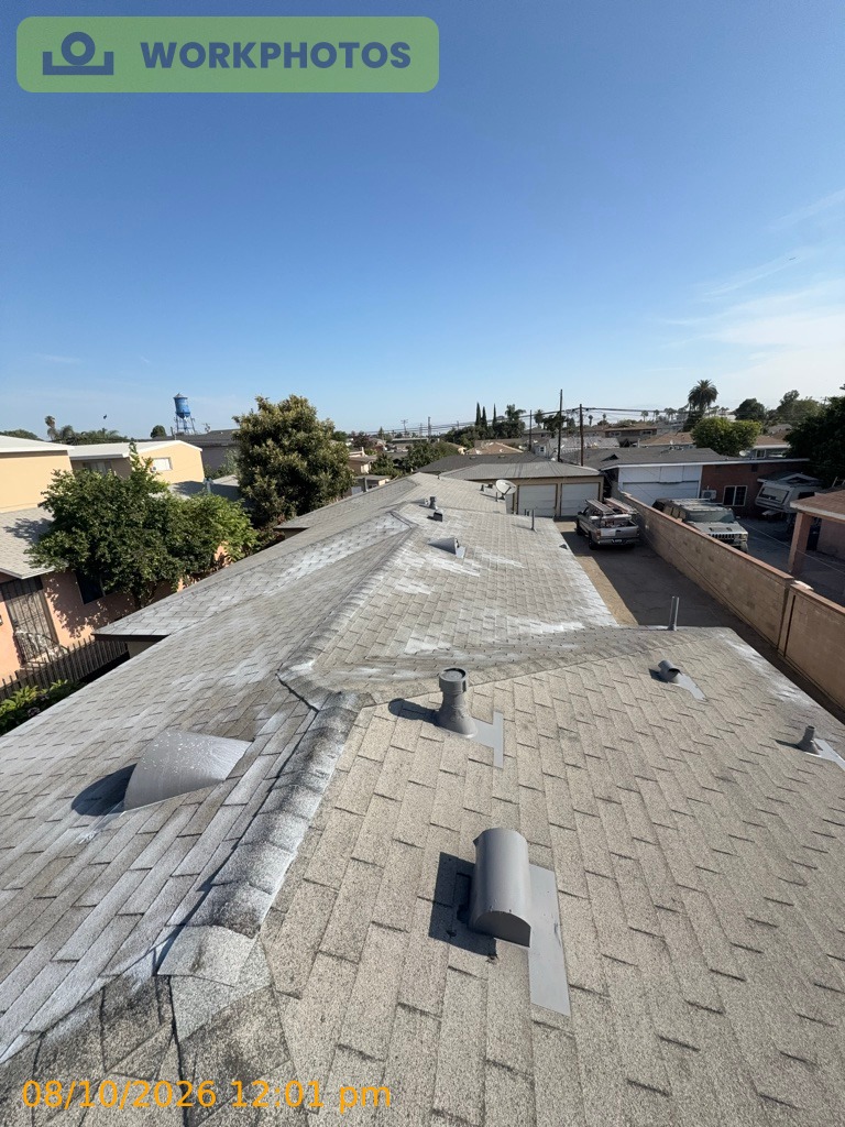 Lynwood multiplex roof before restoration: asphalt composition shingles bleached gray by years of sun across low-slope sections, with a dome skylight, dormer vents and pipe boots, and neighboring rooftops behind.